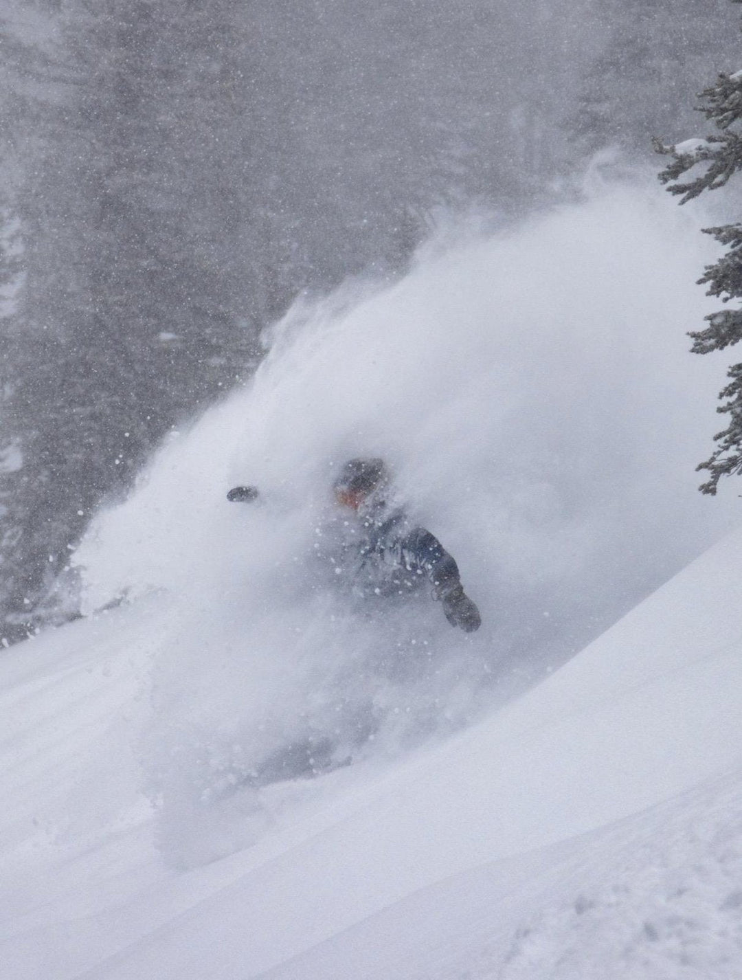 Snowboarder disappearing into a deep powder spray during a storm