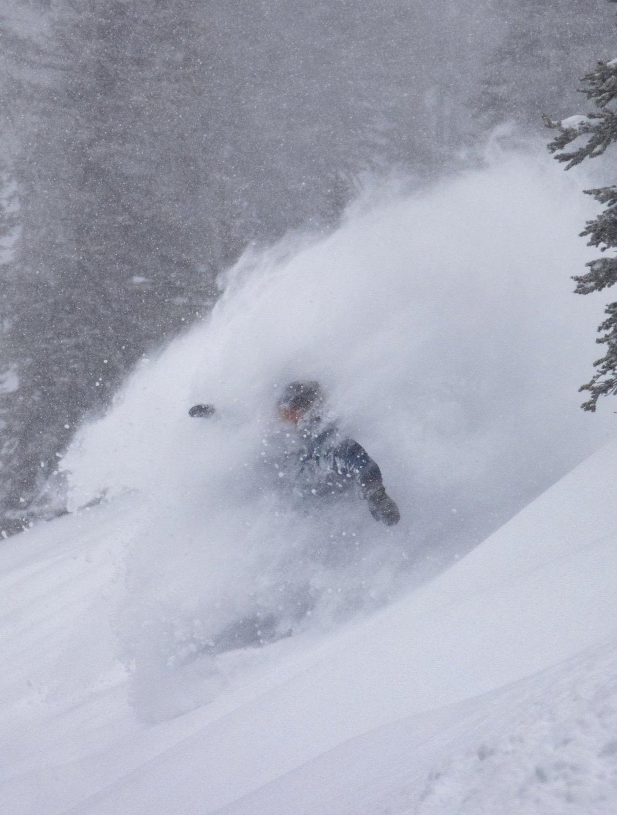 Snowboarder disappearing into a deep powder spray during a storm